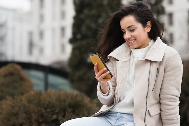 Kostenloses Foto smiley-frau, die telefon im freien betrachtet