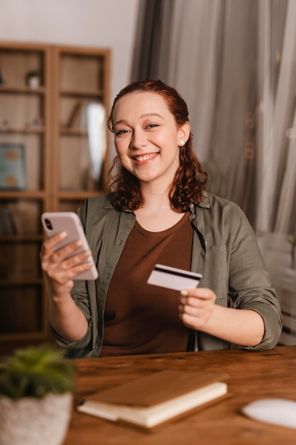 Smiley-Frau mit Kreditkarte und Smartphone zu Hause