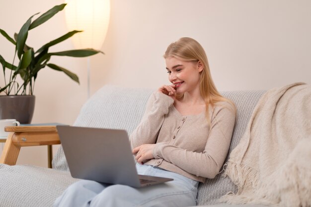 Smiley-Frau mit mittlerem Schuss auf der Couch mit Laptop