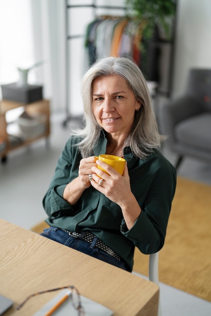 Smiley-Frau mit mittlerem Schuss, die Becher am Schreibtisch hält