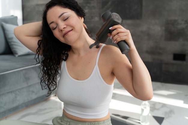 Smiley-Frau mit mittlerem Schuss, die eine Massagepistole verwendet