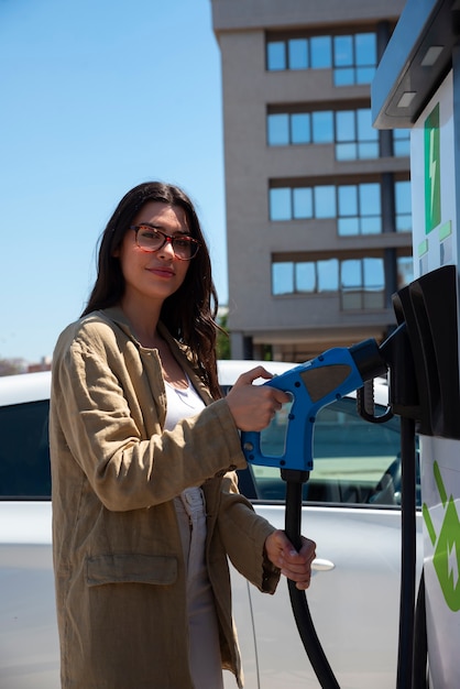 Smiley-Frau mit mittlerem Schuss, die Elektroauto auflädt