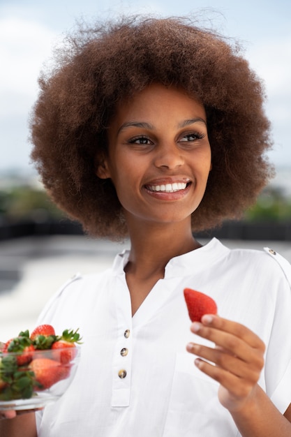 Smiley-Frau mit mittlerem Schuss, die Erdbeeren isst