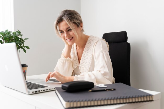 Smiley-Frau mit mittlerem Schuss, die mit Laptop arbeitet