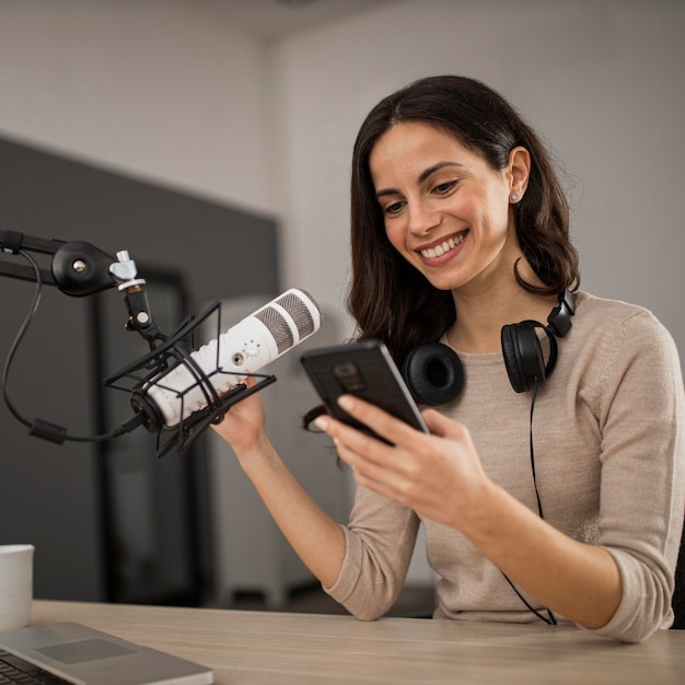 Smiley-Frau mit Smartphone und Mikrofon in einem Radiostudio