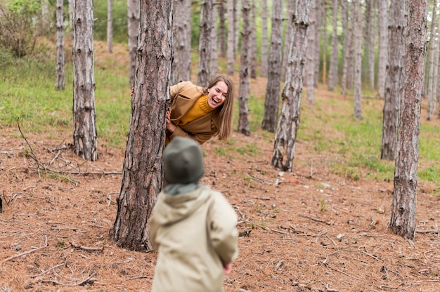Smiley-Frau versteckt sich hinter einem Baum vor ihrem Sohn