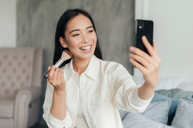 Smiley Frau Vlogging mit einem Make-up Pinsel