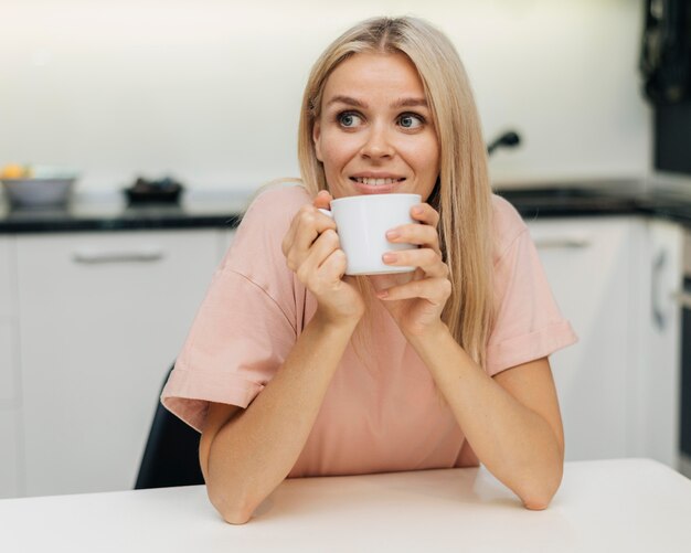 Smiley-Frau zu Hause während der Pandemie, die eine Tasse Kaffee trinkt