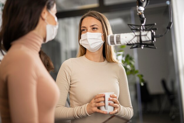 Smiley-Frauen, die zusammen Radio machen, während sie medizinische Masken tragen