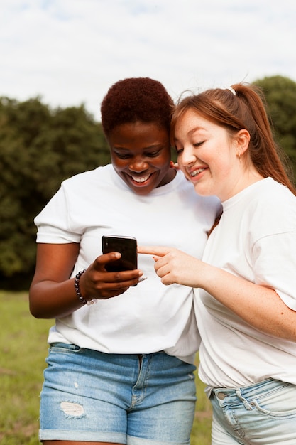 Kostenloses Foto smiley-freundinnen im freien, die smartphone betrachten