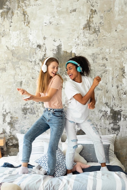 Smiley-Freundinnen tanzen auf dem Bett, während sie Musik über Kopfhörer hören