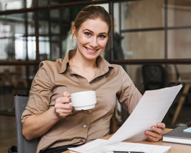 Smiley-Geschäftsfrau, die Kaffee trinkt und Papiere liest