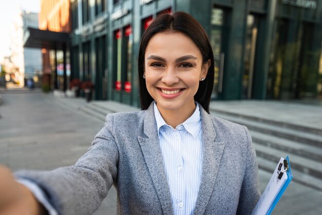 Smiley-Geschäftsfrau mit Zwischenablage, die ein Selfie in der Stadt nimmt