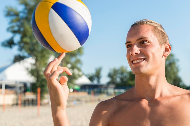 Kostenloses Foto smiley hemdloser männlicher volleyballspieler, der ball mit finger hält