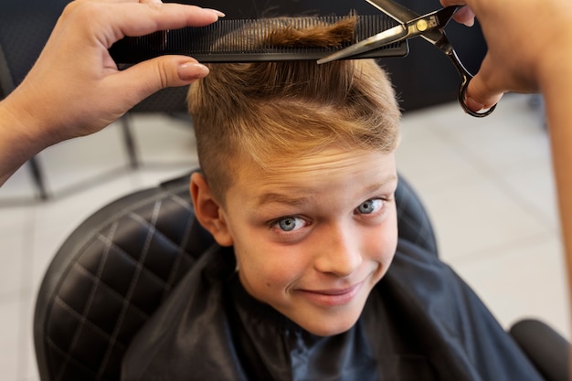 Kostenloses Foto smiley-kind, das einen haarschnitt im hohen winkel des salons bekommt