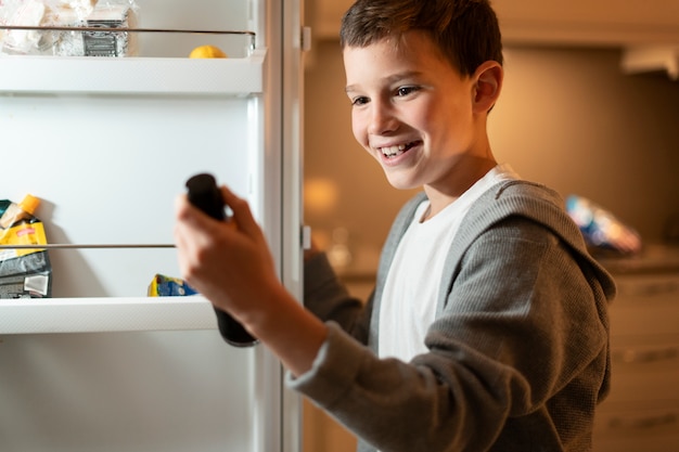 Kostenloses Foto smiley-kind mit offenem kühlschrank hautnah