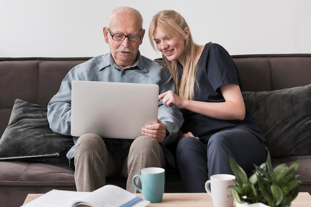 Smiley-Krankenschwester zeigt dem alten Mann den Laptop