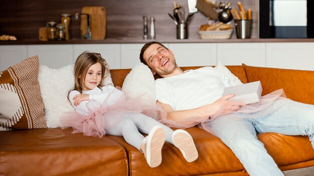 Smiley-Mädchen im Tutu-Rock und Vater, der auf dem Sofa ruht