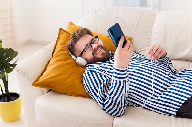 Smiley-Mann auf Sofa, der Musik auf Smartphone genießt