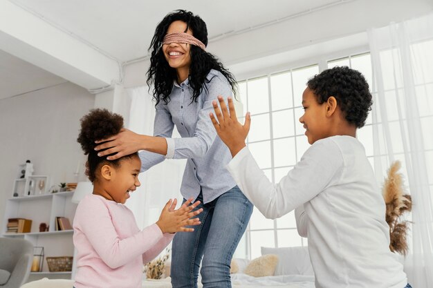 Smiley-Mutter spielt mit verbundenen Augen zu Hause mit ihren Kindern