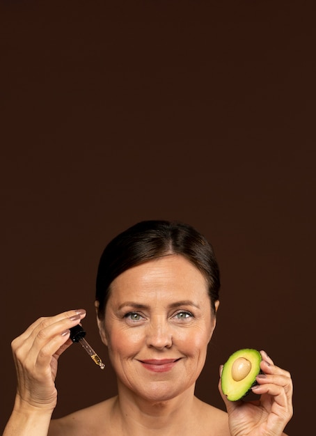 Kostenloses Foto smiley reife frau, die die hälfte einer avocado mit serum und kopienraum hält