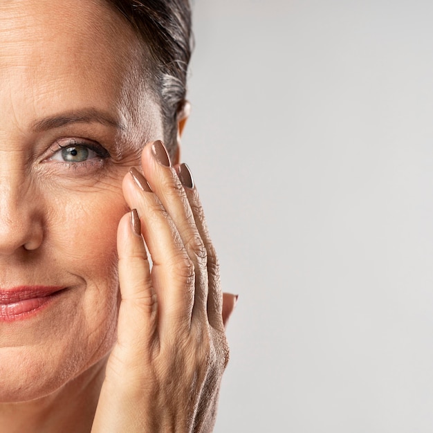 Smiley reife Frau mit Make-up auf posieren mit der Hand auf Gesicht