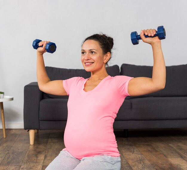 Smiley schwangere Frau, die mit Gewichten trainiert