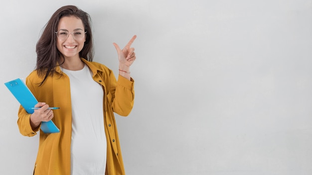 Kostenloses Foto smiley schwangere frau, die zwischenablage hält und mit kopienraum nach oben zeigt