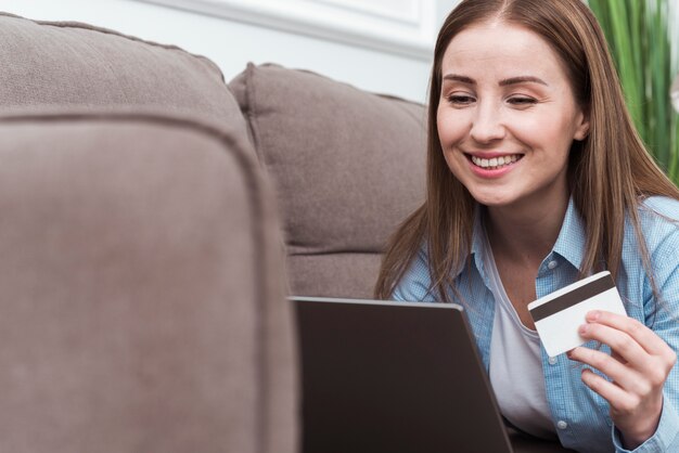 Smileyfrau, die auf Couch sitzt und Kreditkarte hält