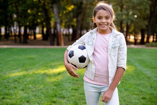 Smileymädchen, das Kamera betrachtet und Ball hält