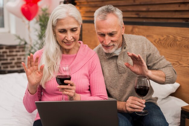 Smileypaare unter Verwendung des Laptops und des trinkenden Weins