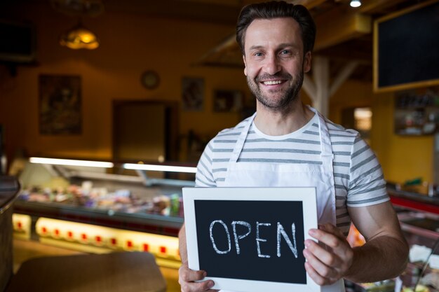 Smiling Besitzer ein offenes Zeichen in der Bäckerei halten