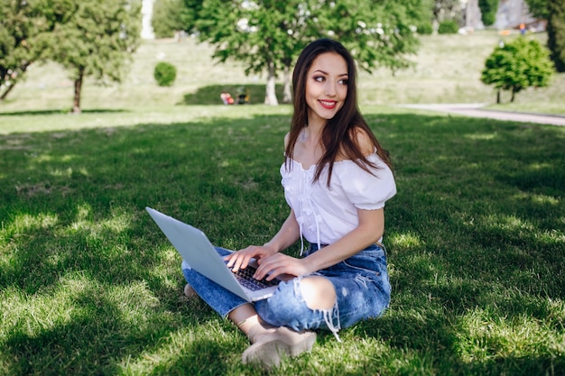 Smiling Mädchen in einem Park auf ihrem Laptop schreibt sitzen