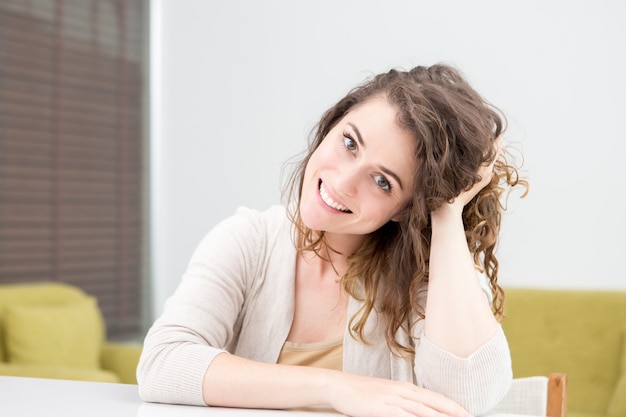 Smiling Wavy-haired Frau sitzt am Tisch zu Hause