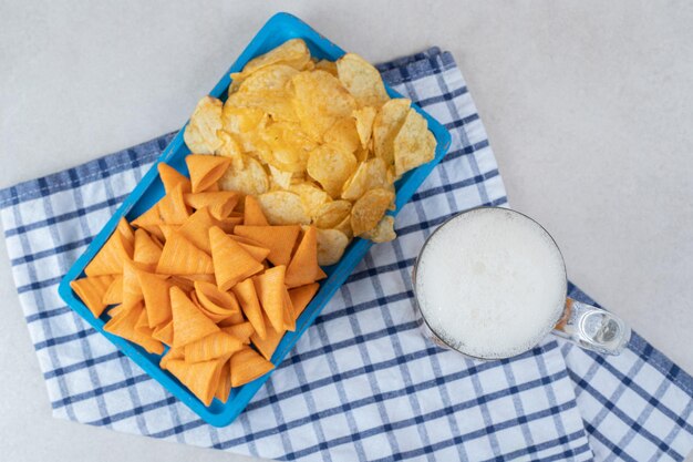 Snackplatte und Glas Bier auf Tischdecke.