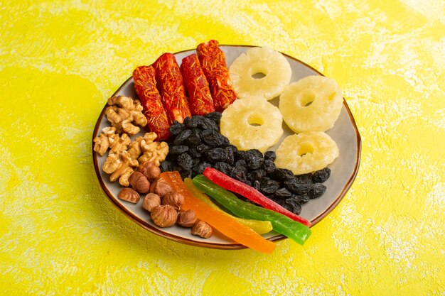 Snackzusammensetzung mit getrockneten Früchten, Nougatnüssen und Ananasringen in der Platte auf Gelb