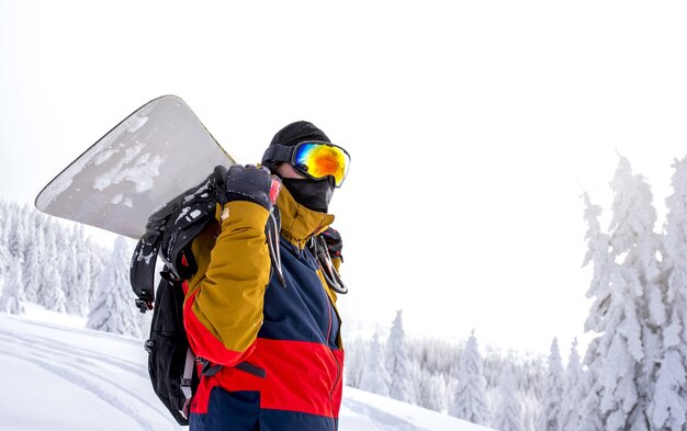 Snowboarder in Schutzbrille hält sein Snowboard auf dem Rücken