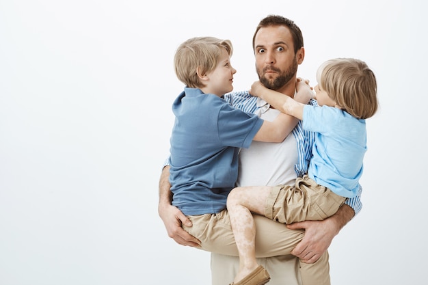 Söhne nutzen den liebevollen und fürsorglichen Vater. Porträt des ahnungslosen lustigen europäischen Vaters, der Kinder auf Händen hält und ahnungslos blickt