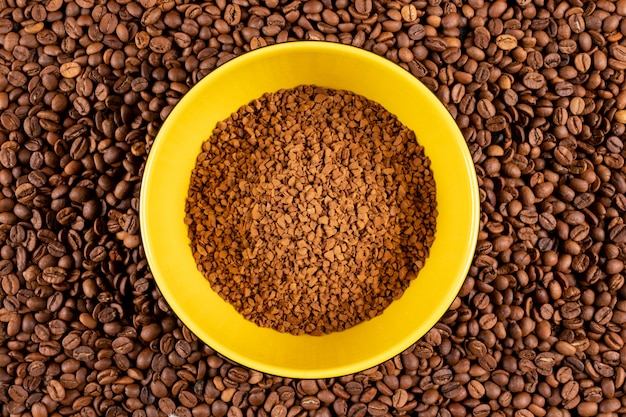 Sofortiger Kaffee der Draufsicht in der gelben Platte auf Kaffeebohnen tauchen auf