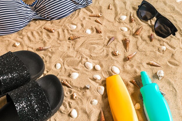 Sommer Bikini und Accessoires stylisches Strandset, Strand Bikini Sommer Outfit und Meersand als Hintergrund, Draufsicht, Konzept