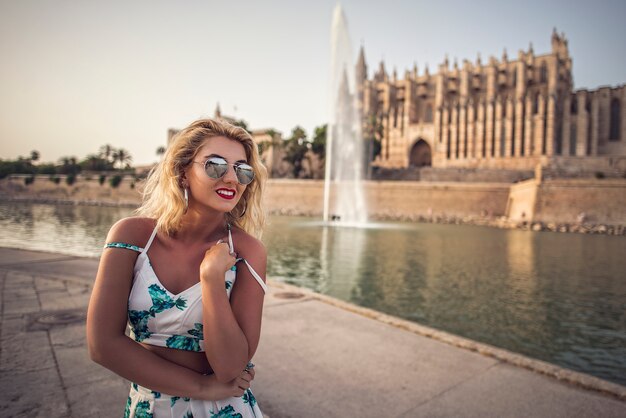 Sommer sonnigen Lebensstil Mode Porträt der jungen stilvollen Hipster Frau posiert auf Straßen, tragen süße trendy weiße Outfit. Frau genießt das Reisen in der europäischen Stadt