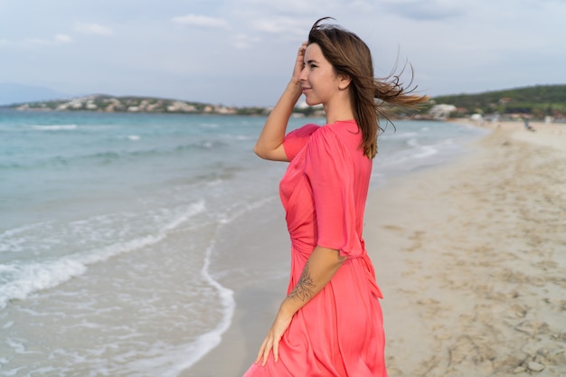 Sommerbild der glücklichen sexy Frau im herrlichen rosa Kleid, das auf dem Strand aufwirft.