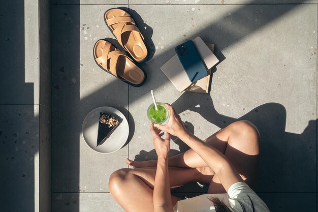 Sommerkomposition mit Hausschuhe Bücher Kuchen und Limonade in weiblichen Händen