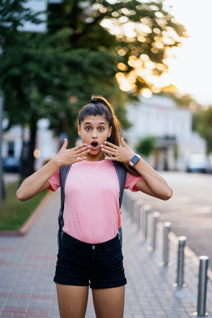 Sommerlebensstil-Modeporträt der jungen überraschten Frau, die auf der Straße geht