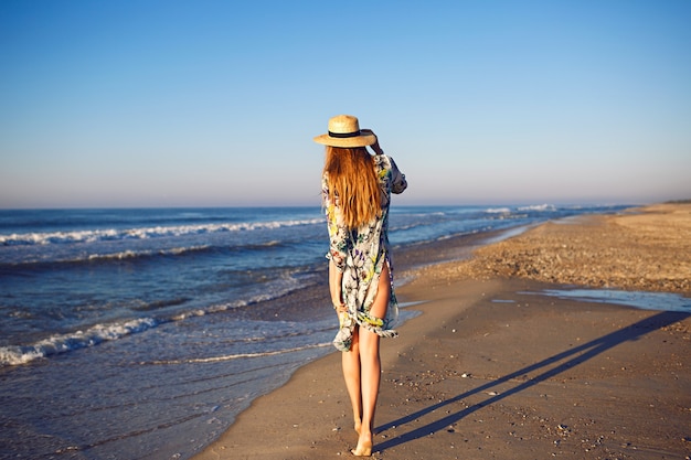 Sommermodeporträt im Freien des blonden Modells, das nahe Ozean am einsamen Strand, getönten Farben, entspannenden Luxusurlaub aufwirft