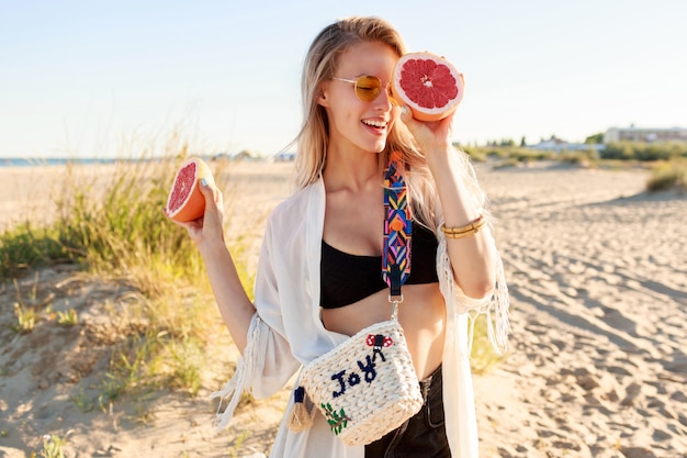 Sommerporträt der verspielten sorglosen Frau, die mit den leckeren Grapefruithälften in den Händen aufwirft.