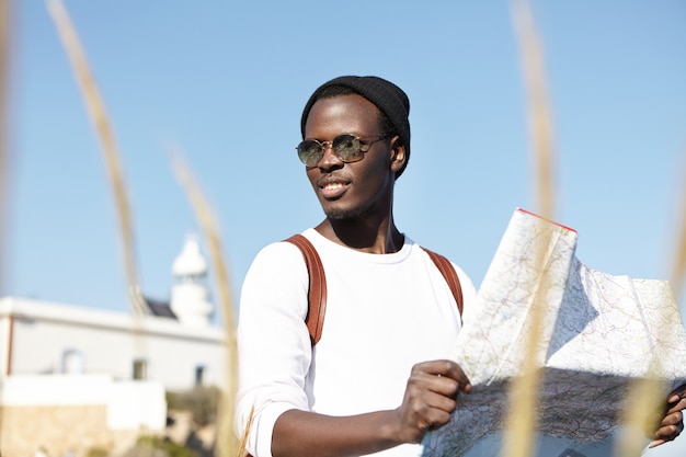 Sommerporträt des jungen Mannes, der Stadtführer beim Sightseeing im Ferienort verwendet
