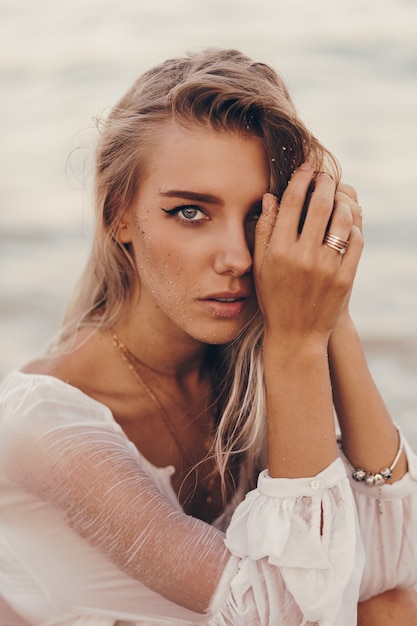 Sommerporträt im Freien der schönen glücklichen blonden Frau, die am Strand nahe Ozean kühlt