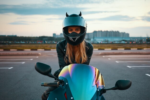 Sommerporträt im Freien der schönen glücklichen jungen Frau, die Sicherheitsmotorradhelm und Lederjacke bereit für Abendfahrt trägt