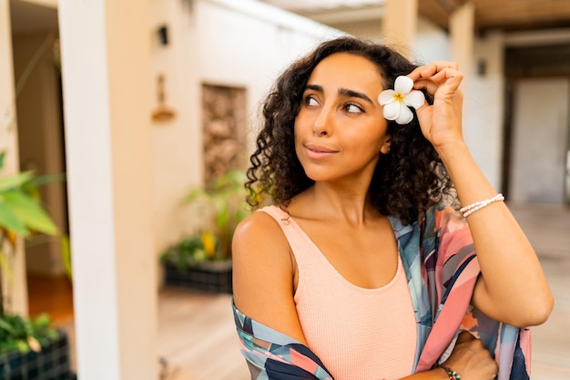 Sommerporträt im Freien einer hübschen brünetten Frau mit tropischer Blume in den Haaren, die im Spa-Hotel posiert